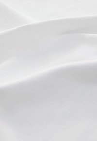 Tissu blanc avec une texture lisse, présentant de douces ondulations et un éclat minimal, indiquant un matériau léger et respirant.