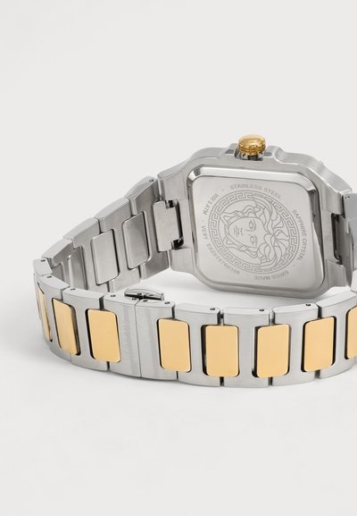 Bracelet de montre en métal argenté et doré avec un fond carré en acier inoxydable gravé d’un logo représentant une tête de Méduse et des marquages suisses.
