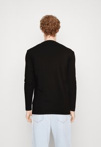 Svart langermet t-skjorte, tettsittende design, rund hals, glatt tekstur; brukt med lyseblå jeans, subtile sømdetaljer synlige.
