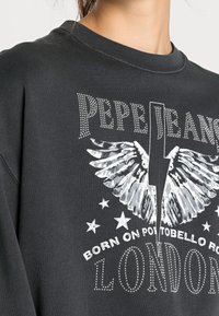 Felpa nera con design grafico che presenta un fulmine, ali, stelle e testo in bianco con dettagli in strass. Collo rotondo.