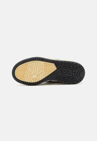 Sorte og beige sneakersåle med en teksturert gummioverflate, som har et sirkelmønster og sikksakkgrep for bedre feste.