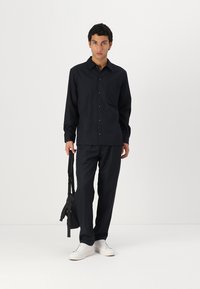 Navy button-up shirt and matching pants, slim fit, cotton blend fabric, chest pocket, paired with white sneakers and a black bag.