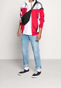 Röd och vit zip-up jacka med marinblå detaljer, vit t-shirt, ljusblå uppvikta jeans och svarta kanvas sneakers med vita sulor.