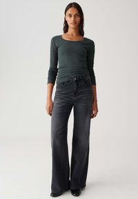 Donkergrijze wijde jeans, gecombineerd met een aansluitend, langemouwen donkergroen top met een ronde hals en geribbelde textuur.
