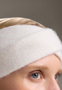 Ensemble de bandeau tricoté blanc en matériau doux, avec un design tordu qui couvre le front et une texture lisse.