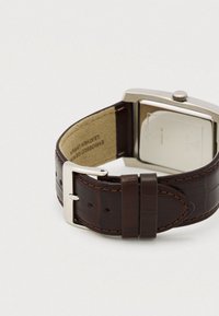 Καφέ δερμάτινο λουράκι ρολογιού με σχέδιο κροκόδειλου, ασημένια θήκη από ανοξείδωτο ατσάλι και απλό κούμπωμα. Υφασμένο εσωτερικό επένδυση.