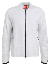 Veste blanche Nike zippée avec manches texturées, fermeture éclair noire et poignets, et poches latérales zippées, vue de face.