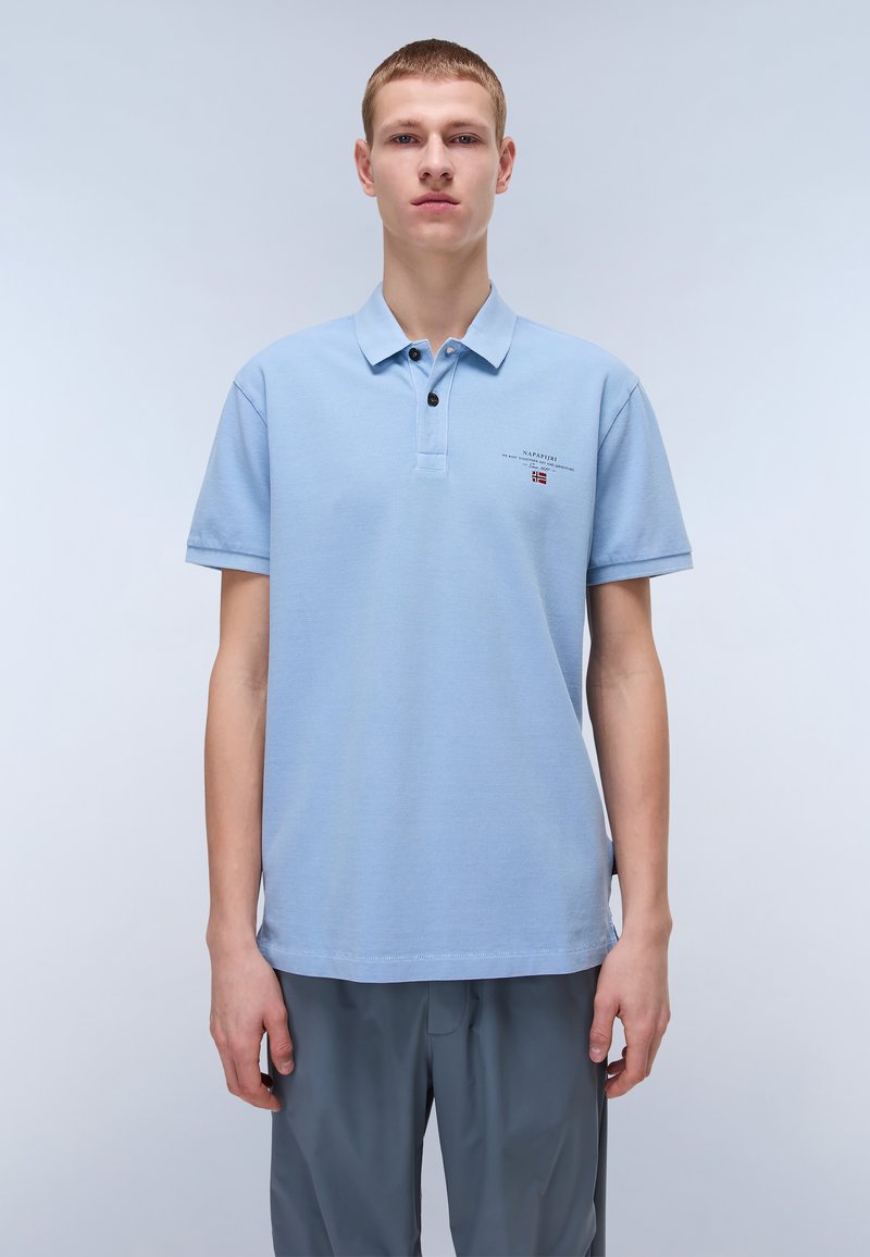 Polo shirt celeste con maniche corte, chiusura a due bottoni e piccolo logo. Il tessuto sembra strutturato e traspirante.