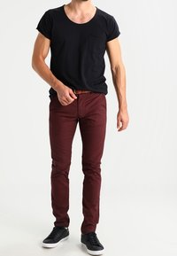 Svart kortärmad t-shirt med ficka, i kombination med smala burgundy byxor och svarta sneakers. Slät tyg, enkel design, inga mönster.