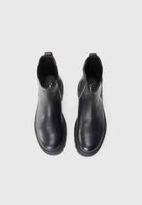 Bottines noires en cuir avec une texture lisse, des panneaux latéraux élastiques et une semelle épaisse. Présente une semelle intérieure de marque avec le texte "Calvin".