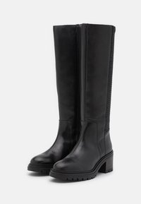 Bottes noires en cuir montant jusqu'aux genoux avec un talon épais, présentant un panneau latéral texturé et une finition lisse à l'avant.