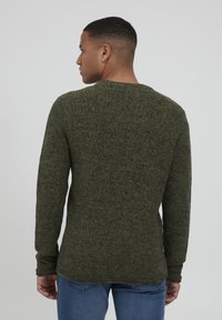 Strikkegenser i mørkegrønn med teksturert mønster, rund hals og lange ermer, kombinert med bl�å jeans. Vist fra bak.