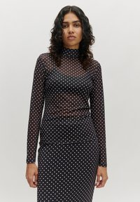 Schwarze, transparente Langarmbluse mit weißen Punkten, versehen mit einem hohen Kragen und einer taillierten Passform, kombiniert mit einem gepunkteten Rock.