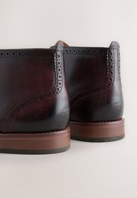 Dunkelburgunderrote Lederstiefel mit perforierten Details, glattem Finish und einem gestapelten Holzabsatz. Verfügt über ein schlankes, abgerundetes Profil.