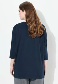 Marinblus, långärmad topp med rund halsringning och sidoklipp, tillverkad av mjukt, lättviktigt tyg. Bakvyn visar en jämn textur och naturligt fall.