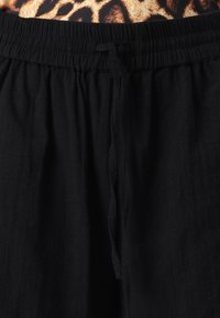 Black drawstring pants with a gathered elastic waistband. Soft, textured fabric with a relaxed fit, featuring a tie at the front.