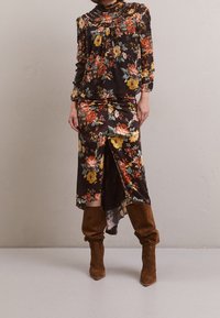 Robe à imprimé floral sur fond sombre, avec un col froncé et une fente haute. Associée à des bottes en daim marron montant jusqu'au genou. Texture de tissu lisse.