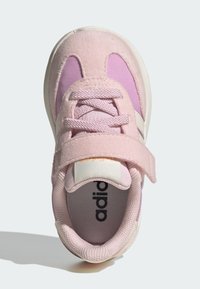 Světlé růžové tenisky pro batole s suchým zipem, textilními tkaničkami, polstrovaným límcem a částečně viditelným černým textem uvnitř boty.