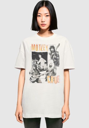 T-shirt oversized blanc avec des images en noir et blanc de musiciens et le texte orange "MÖTLEY CRÜE". Manches courtes, col rond.