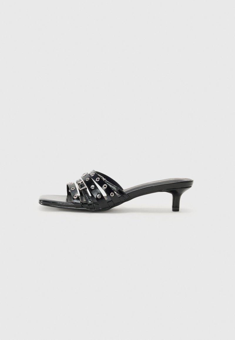 Black heeled sandals with multiple glossy straps and metallic accents, featuring a pointed toe and modest kitten heels. Smooth texture.