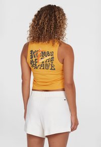 Yellow sleeveless crop top with black text and graphic on the back, paired with white soft shorts featuring a stitched hem detail.