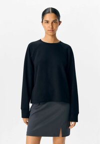Sort sweatshirts med lange raglanærmer, rund halsudskæring og en afslappet pasform, der er parret med en grå nederdel med en sideslids.