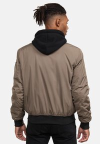 Giacca bomber da uomo in khaki, con cappuccio nero, polsini e orlo a coste. Tessuto liscio e leggero con una silhouette aderente.