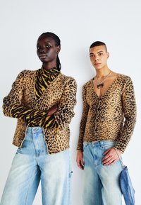Luipaardprint, gebreide cardigan in tan en zwart; met lange mouwen en een V-hals. Gepromoot met lichtblauwe jeans. Model draagt een tijgergestreept top.