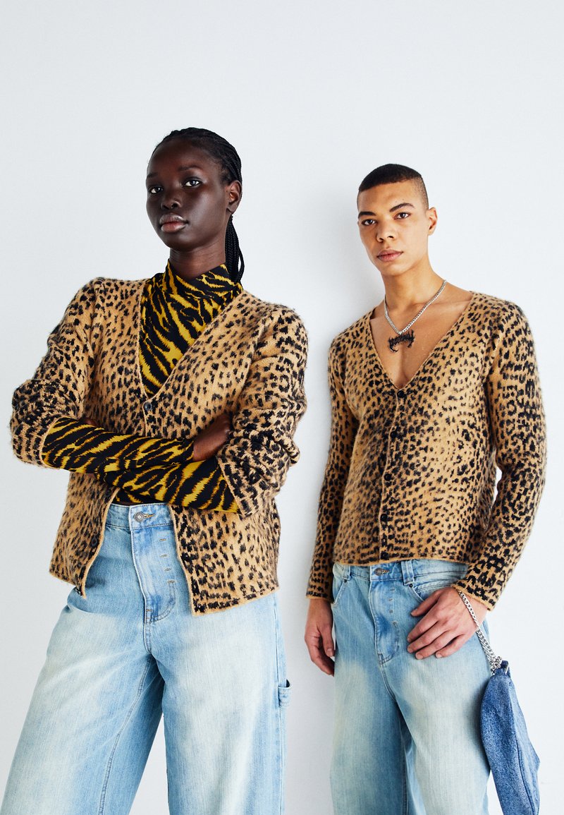 Luipaardprint, gebreide cardigan in tan en zwart; met lange mouwen en een V-hals. Gepromoot met lichtblauwe jeans. Model draagt een tijgergestreept top.
