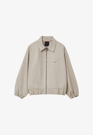 Veste légère beige avec zip, coupe oversize, poignets et ourlet élastiqués, dotée d'une petite poche sur la poitrine avec un rabat pointu.