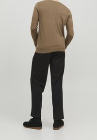 Pull tricoté marron, col rond, ourlet côtelé, porté avec un pantalon noir et des chaussures en daim noir, vu de dos. Texture lisse.