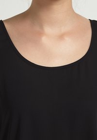Top nero senza maniche con scollatura ampia a barca. Tessuto morbido e liscio con una texture leggera. Design semplice e sobrio.