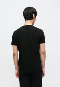 Fekete pamut póló kerek nyakkivágással és rövid ujjakkal. A hátoldali nézet sima textúrát és klasszikus szabást mutat.