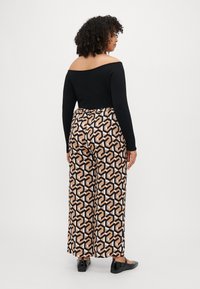 Zwarte off-the-shoulder top gecombineerd met gemusterde wijde broeken met geometrische vormen in zwart, beige en cream. Plat zwart schoeisel.