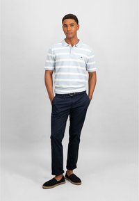 Polo shirt rayé bleu clair avec col, associé à un pantalon sombre et des espadrilles noires. Présente un petit logo sur la poitrine.