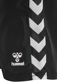 Svarta sportshorts med ett vitt chevron-mönster längs sidan, med ett andningsbart nätpanel och en diskret logotyp.