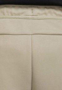 Beige Sweatpants aus einem glatten, strukturierten Stoff. Verfügt über einen dehnbaren Taillengummi und dezente Nahtdetails auf der Rückseite.