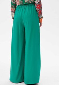 Groene wijde broek met een ontspannen pasvorm en elastische tailleband, gemaakt van soepele, lichte stof zonder zichtbare zakken of patronen.