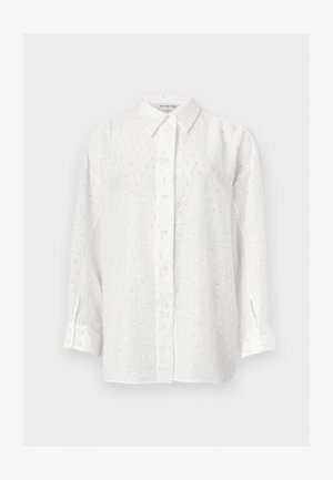 Fehér, hosszú ujjú, gombos ing finom pöttyös flittermintával és klasszikus gallérral, egyszínű háttéren.