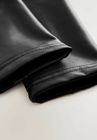 Crne hlače od umjetne kože s glatkom teksturom, preklopnim rubovima i urednim šavovima, koje prikazuju elegantan dizajn.