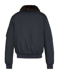 Granatowa kurtka bomberka z prążkowanymi mankietami i dołem, ciemno-brązowym futrzanym kołnierzem oraz kieszeni na rękawie widoczna z tyłu.