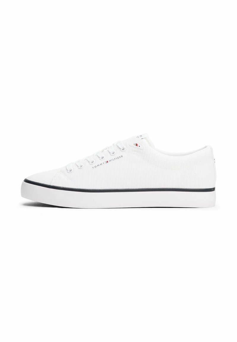 White canvas sneakers with a low top design, featuring round laces, a rubber sole, and a contrasting navy stripe along the bottom edge.