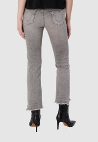 Jeans en denim gris avec une coupe slim, un ourlet effiloché et des poches arrière emblématiques. Associés à des bottines noires à bout pointu.