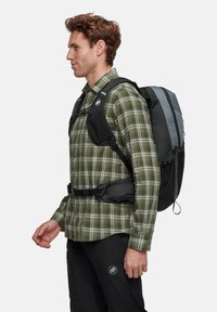 Zaino nero e grigio con un motivo geometrico, spallacci regolabili e una cintura con fibbia in vita. Indossato da una persona con una camicia a quadri.