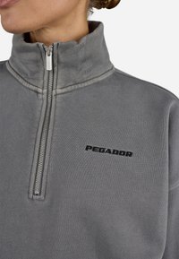 Gray fleece pullover with a high collar, half zipper, and black "PEGADOR" logo. Features visible stitching and soft textured fabric.