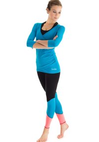 Türkises Langarmshirt kombiniert mit schwarzen Leggings, die an den Knöcheln pinke und blaue Akzente aufweisen. Glattes Material mit figurbetontem Schnitt.