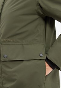 Olivegrüne wasserdichte Jacke mit Reißverschluss, Druckknopfklappen-Tasche, weichem Stoffgefühl und Markennähten.
