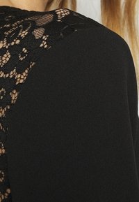 Czarna odzież z koronkowym panelem na plecach, łącząca fakturowaną koronkę z gładkim materiałem, prezentująca skomplikowane wzory na solidnej bazie.