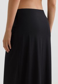 Črna maksi krilo iz gladkega blaga. Ima visok pas in tekočo zasnovo ter subtilen nabrani detajl na zadnji strani.