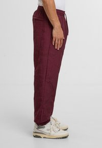 Burgundowe spódnice pikowane z elastycznym pasem, boczną kieszenią, zwężanymi nogawkami i teksturowanym wzorem, zestawione z białymi i szarymi sneakersami.